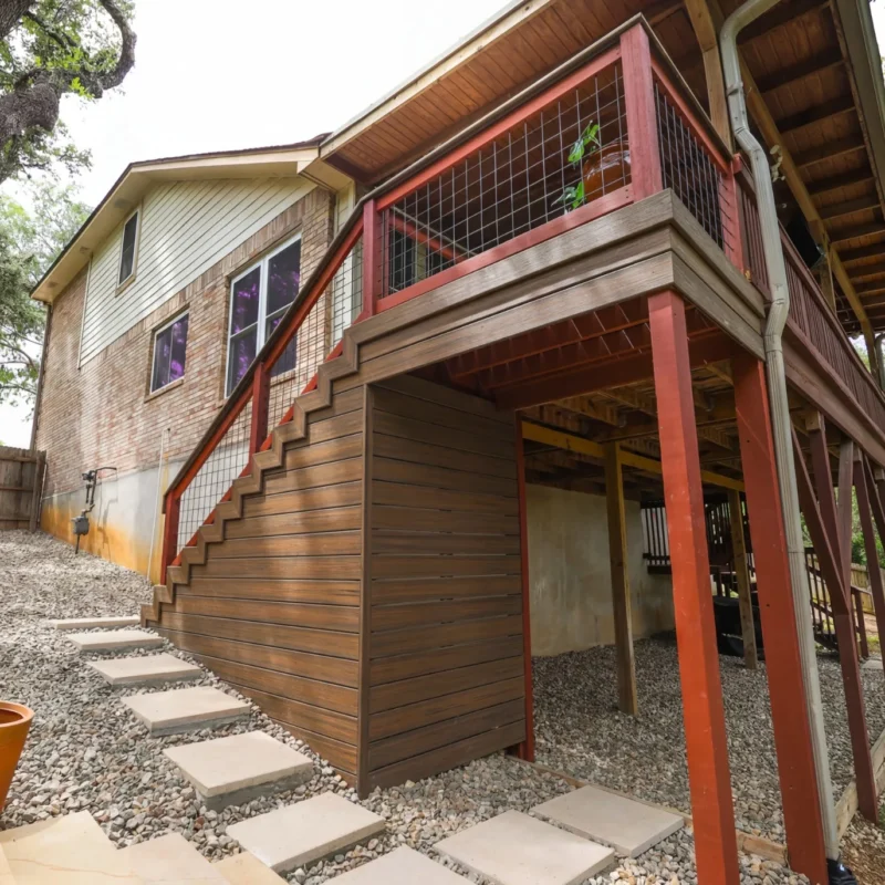 Two-story house with wooden deck and stone path in a landscaped yard