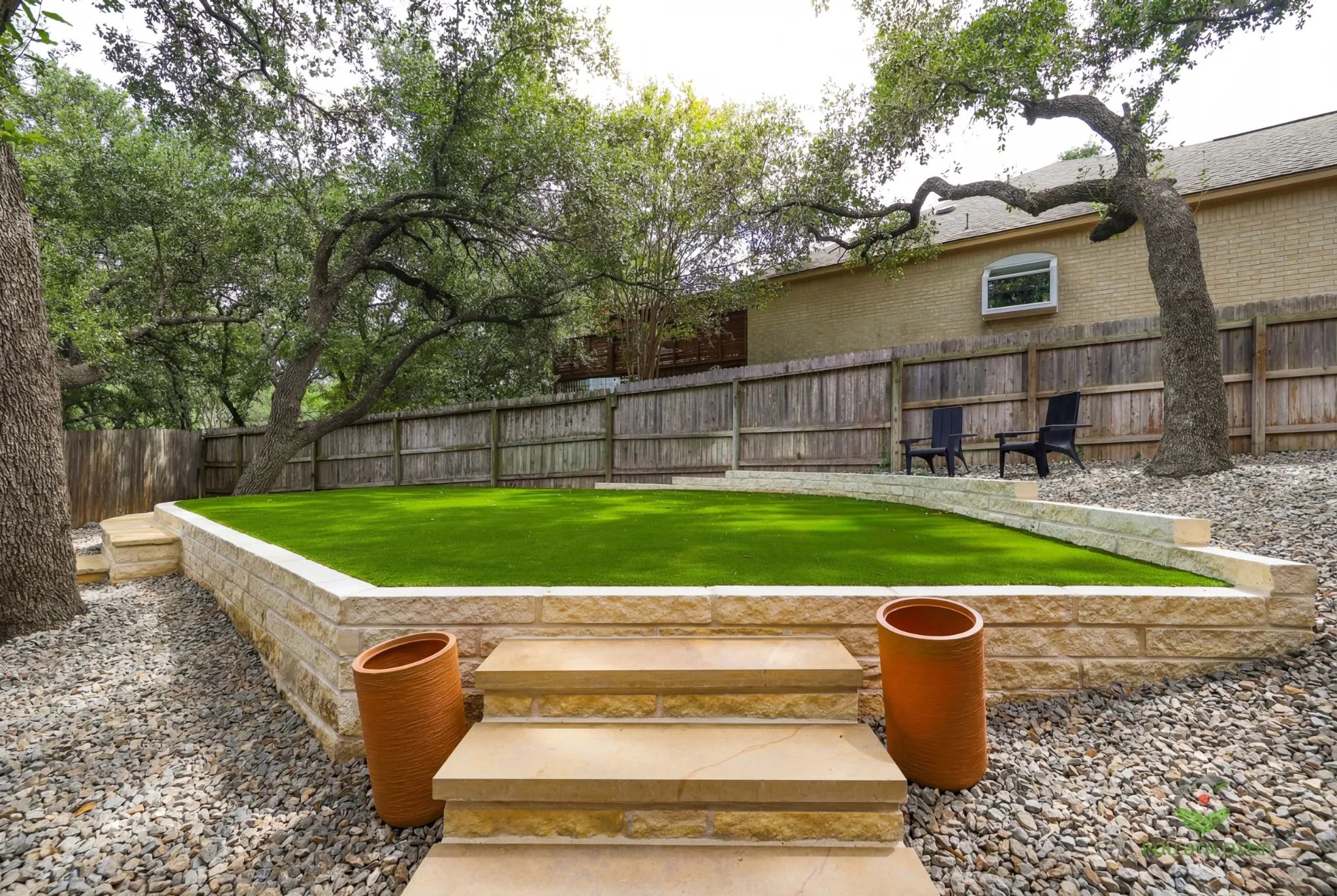 Landscaped backyard with artificial turf, stone steps, and potted plants