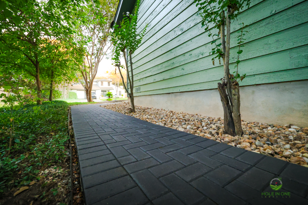 Side-yard charcoal brick paver walkway with river rock strip along siding