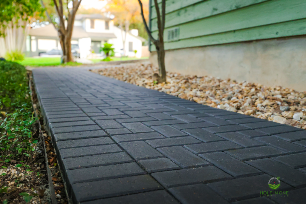 Narrow charcoal paver side-yard path with river rock border beside a green home