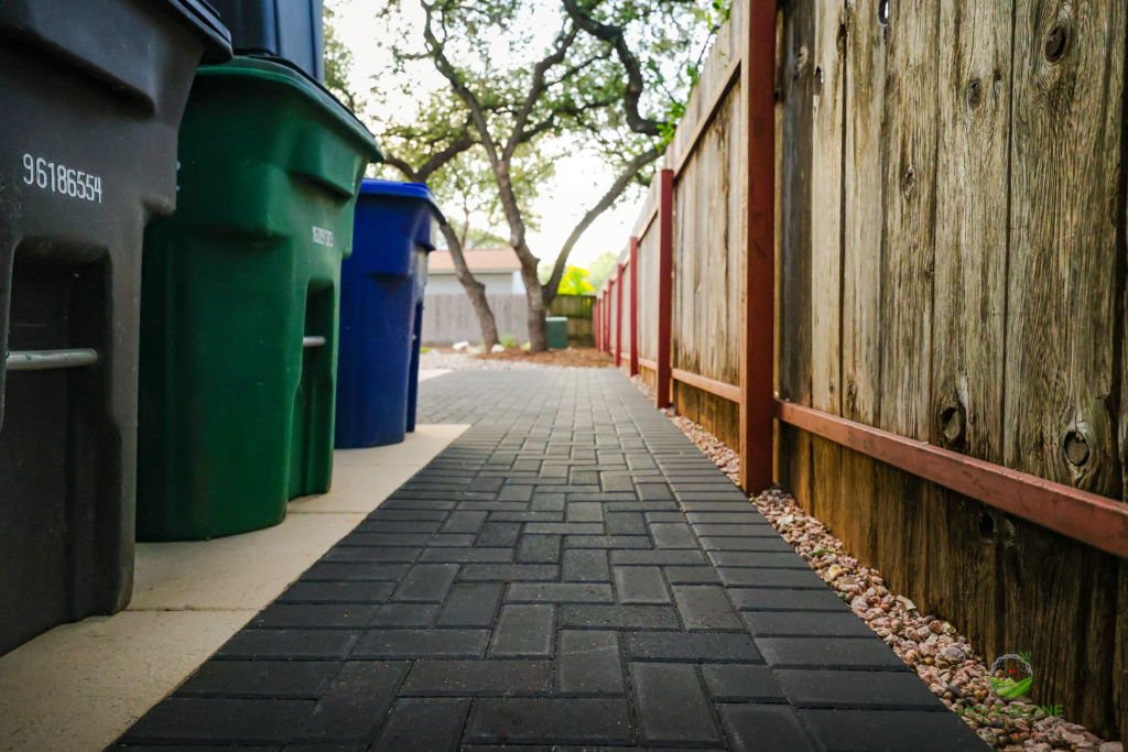 Charcoal paver side-yard walkway with trash bin pad along a cedar fence