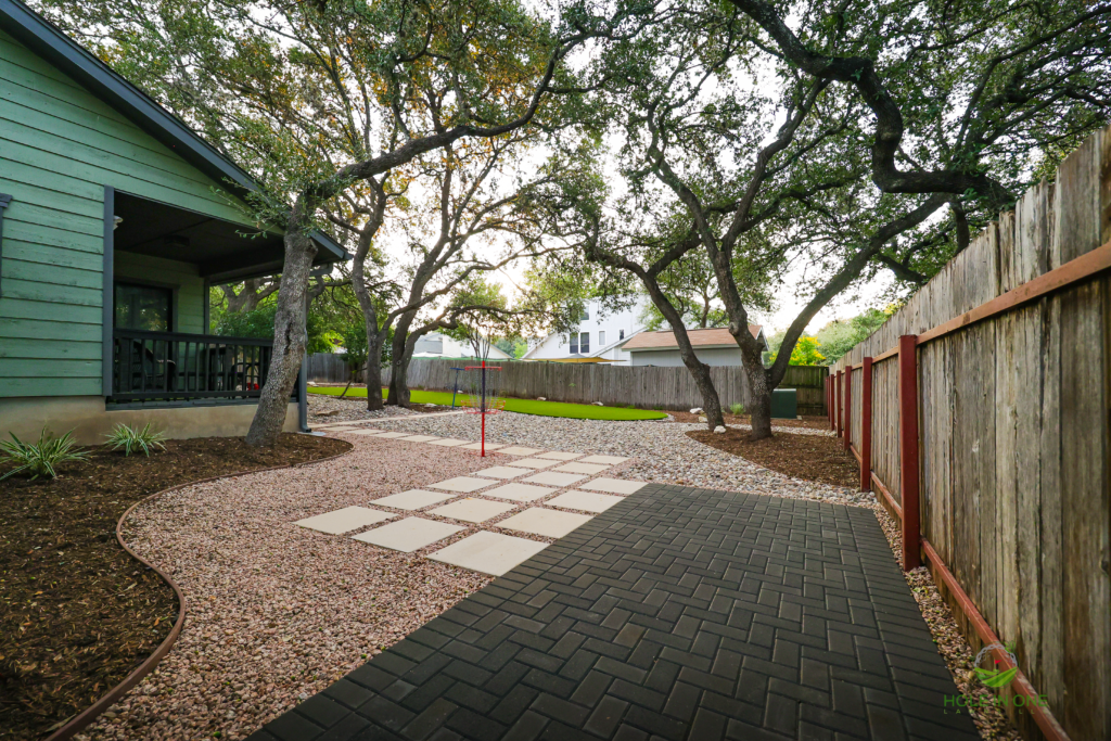 Dark herringbone paver path and gravel area beneath large live oaks