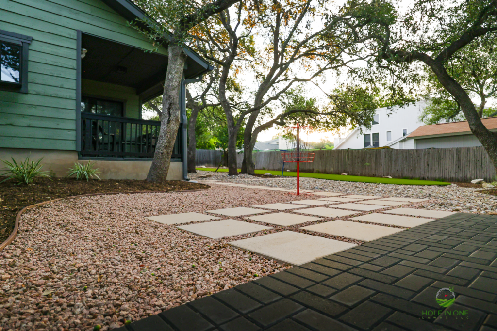 Charcoal paver walkway meeting concrete stepping pads in a gravel backyard