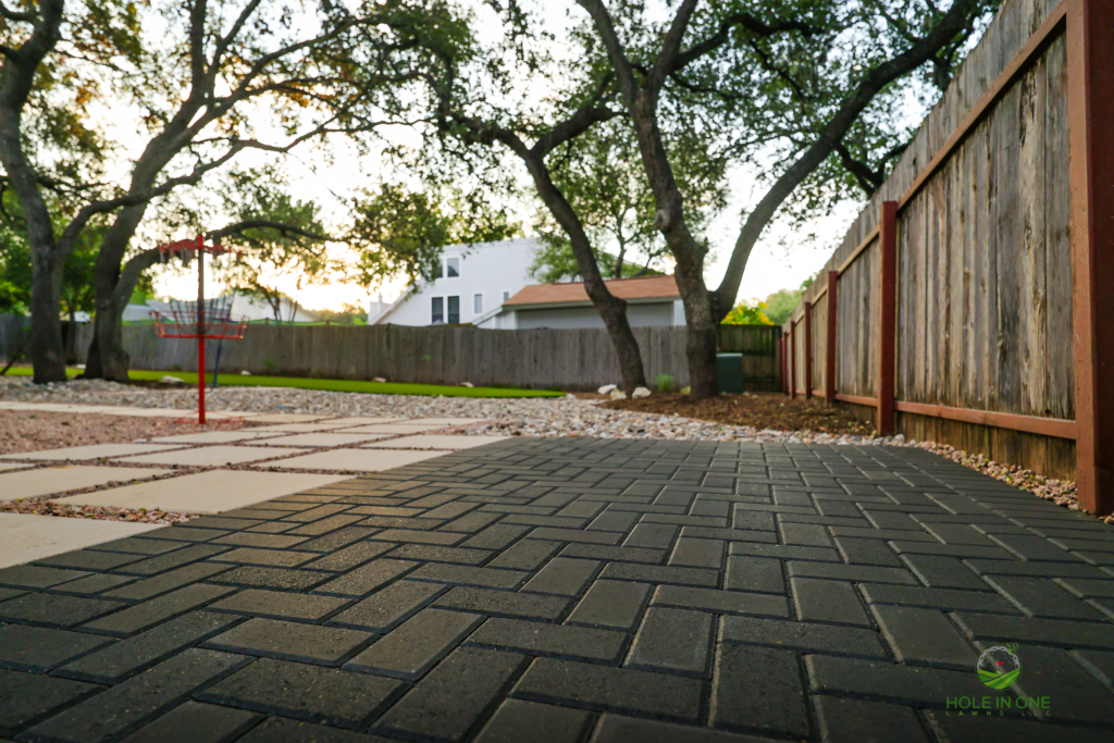 Charcoal brick paver walkway beside a gravel yard under mature oaks