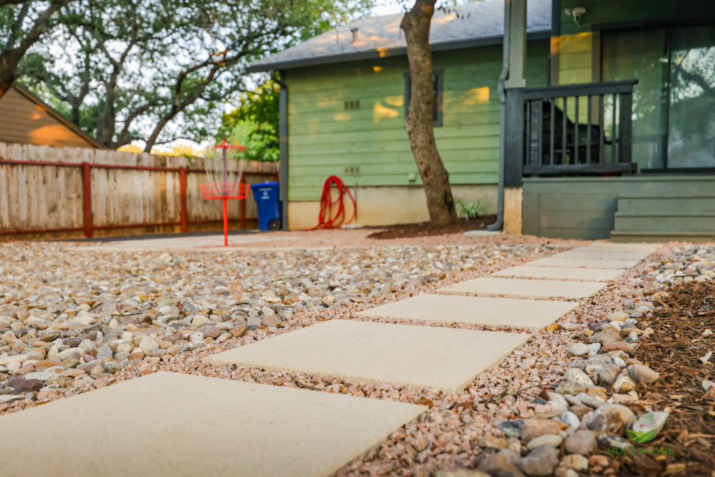 Gravel yard with concrete stepping pads leading to a green craftsman home
