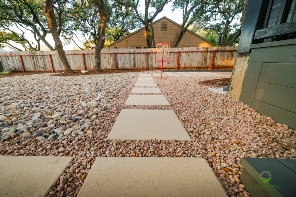 Concrete paver stepping stones in pea gravel aligned toward a disc golf basket