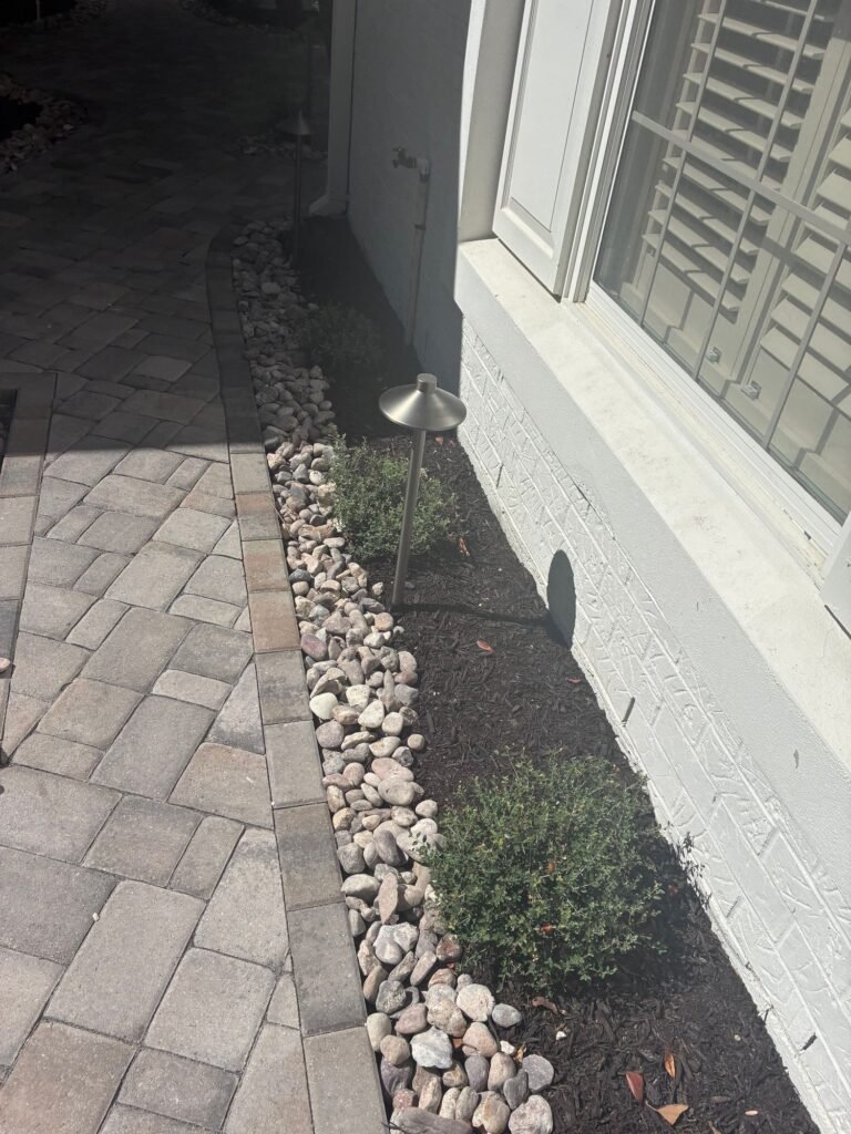 Paver walkway with river rock border, shrub bed and bronze path light along a home in Alamo Heights, TX