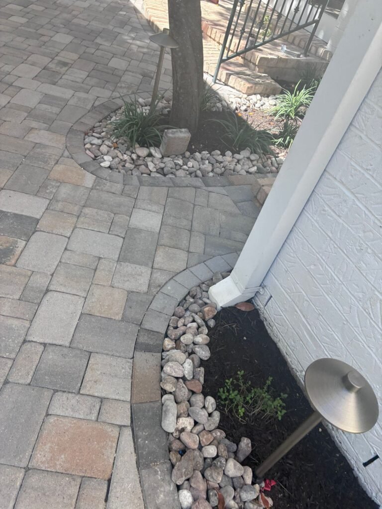 Paver walkway with river rock tree ring and path light near a planting bed at an Alamo Heights home
