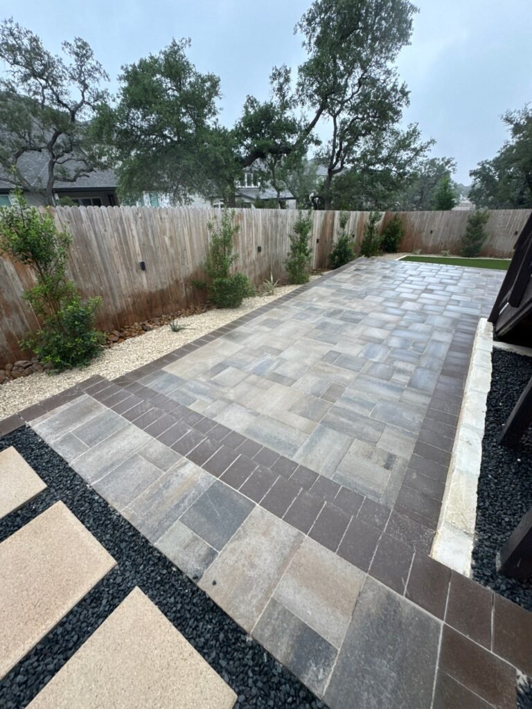 Grey paver patio with charcoal border, stepping pads in black gravel and fence-line plantings in Boerne, TX