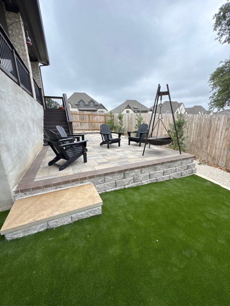 Raised paver patio on a block retaining wall with block step and synthetic turf lawn in a Boerne, TX backyard