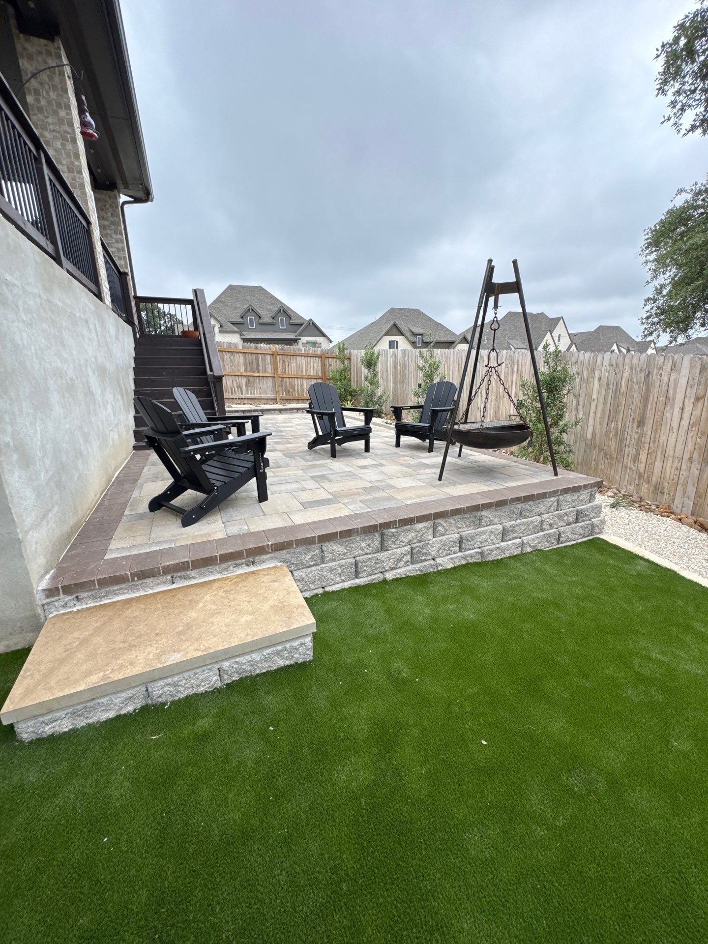 Raised paver patio on a block retaining wall with block steps and artificial turf in Boerne, TX