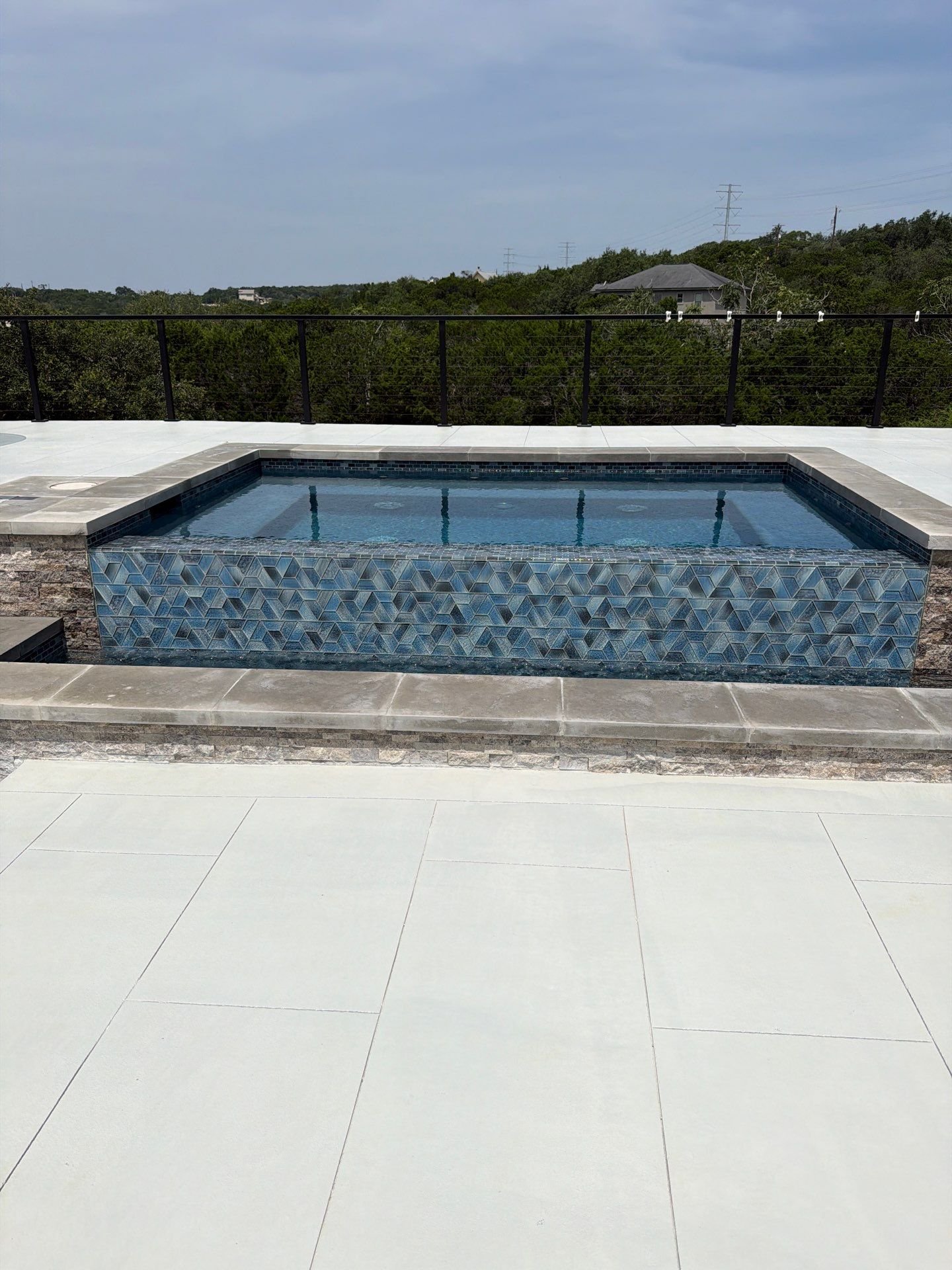 Mosaic-tiled spa with stone coping on a light porcelain paver pool deck in Bulverde, TX
