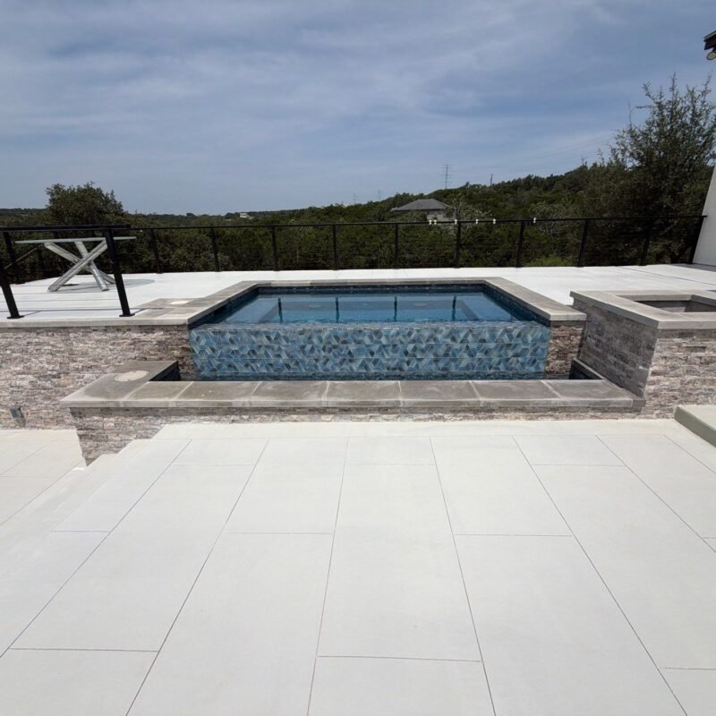 Raised spa with stacked-stone veneer and large-format porcelain paver deck overlooking the Hill Country in Bulverde, TX