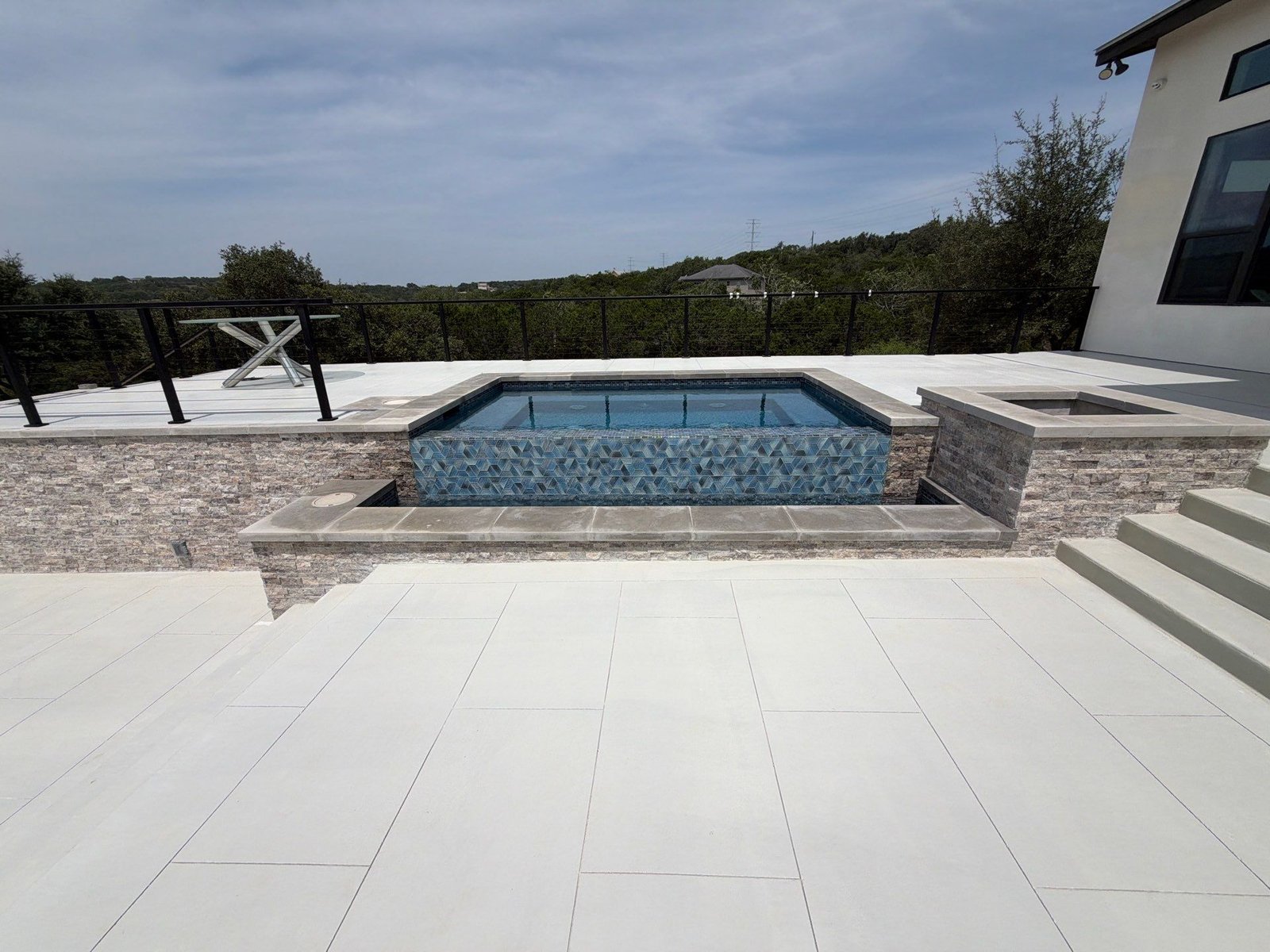 Raised spa with stacked-stone veneer and a porcelain paver pool deck in Bulverde, TX