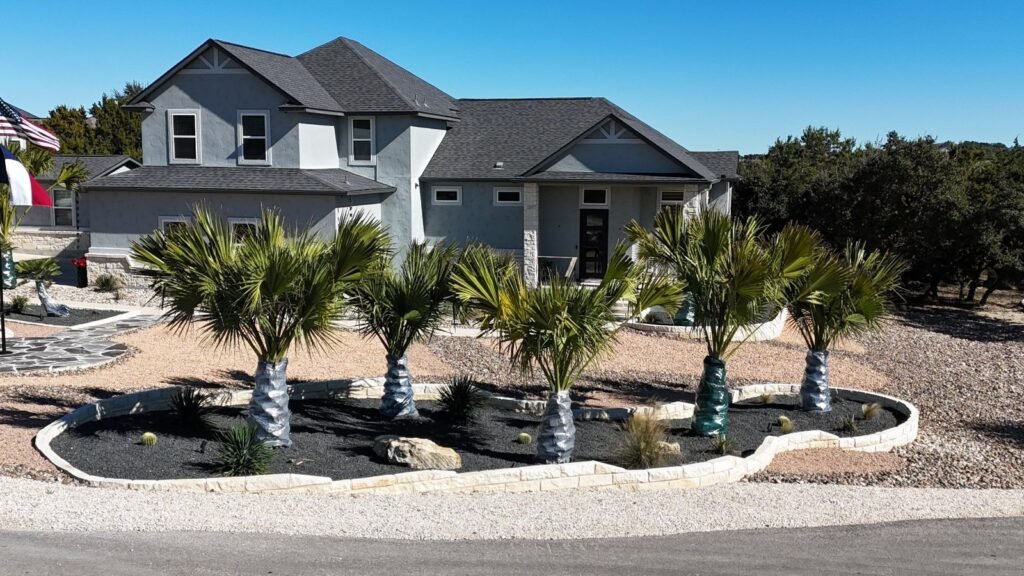 Front-yard xeriscape with curved limestone-bordered beds, palms, boulders and agaves at a Canyon Lake, TX home