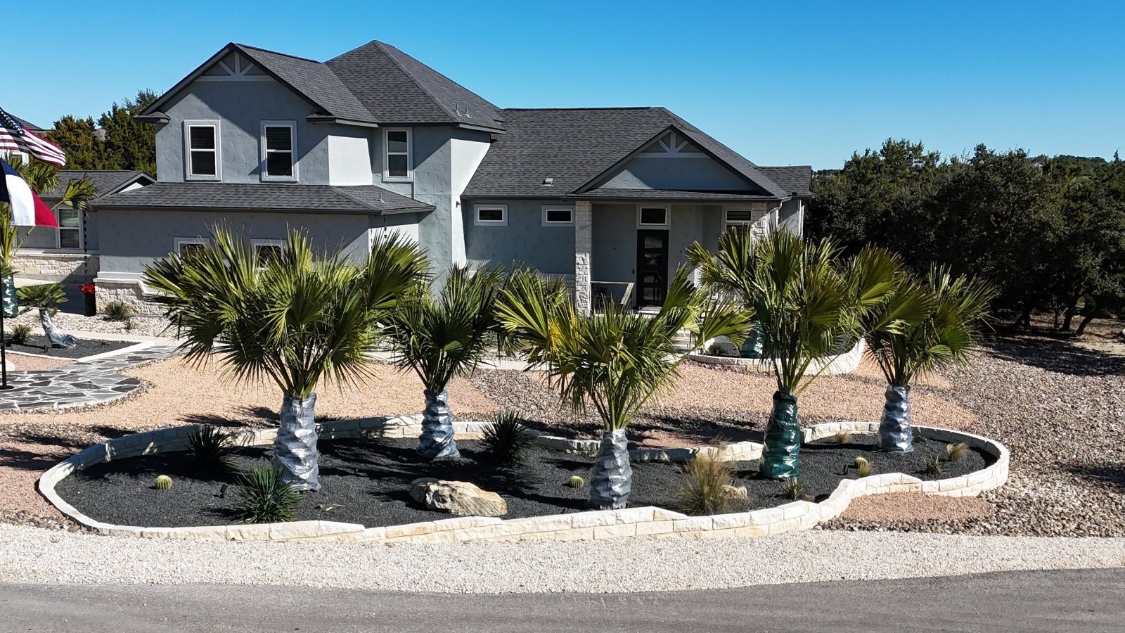 Front-yard xeriscape with curved limestone-bordered beds, palms, boulders and agaves at a Canyon Lake, TX home