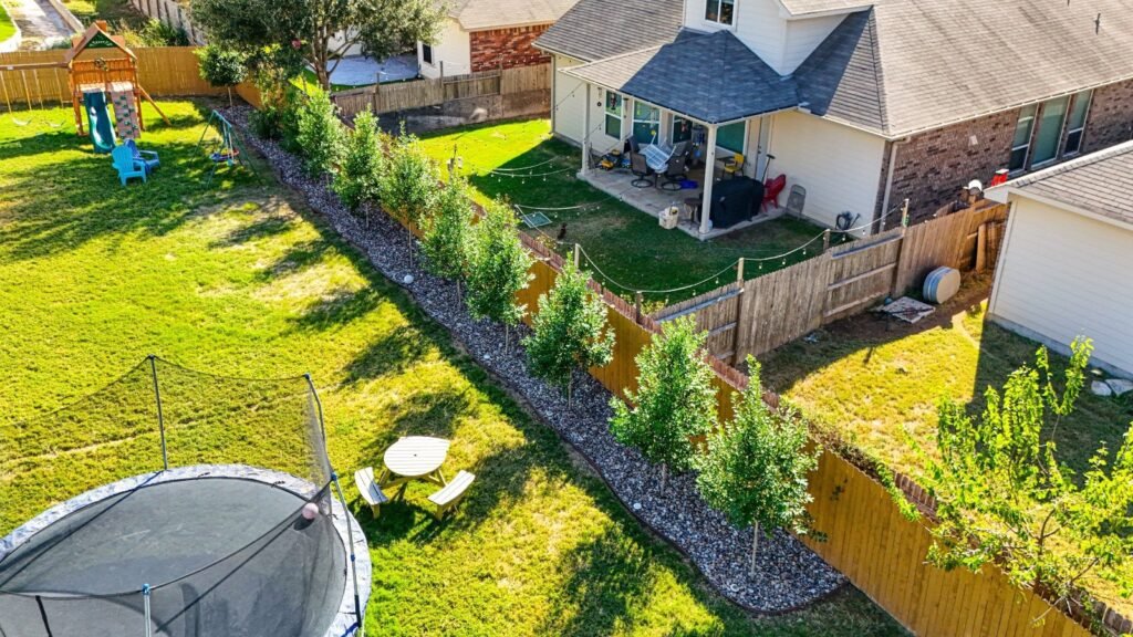 Aerial of a tree-lined rock border, lawn and covered patio at a Cibolo, TX home