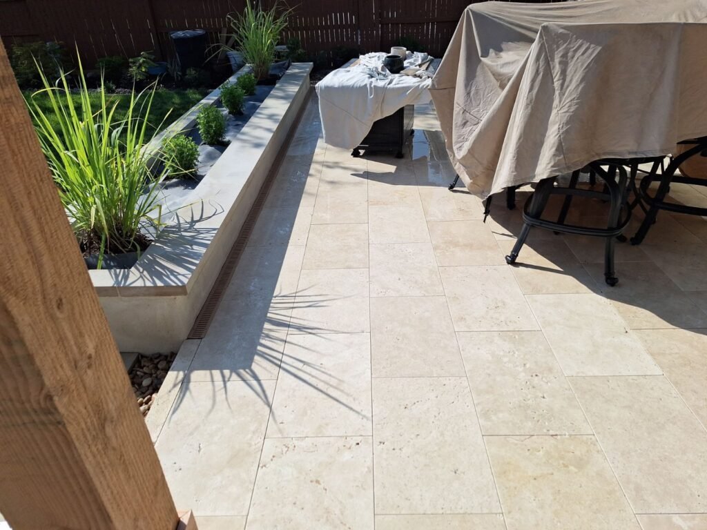 Travertine patio beside a raised planter bed with ornamental grasses in Cibolo, TX