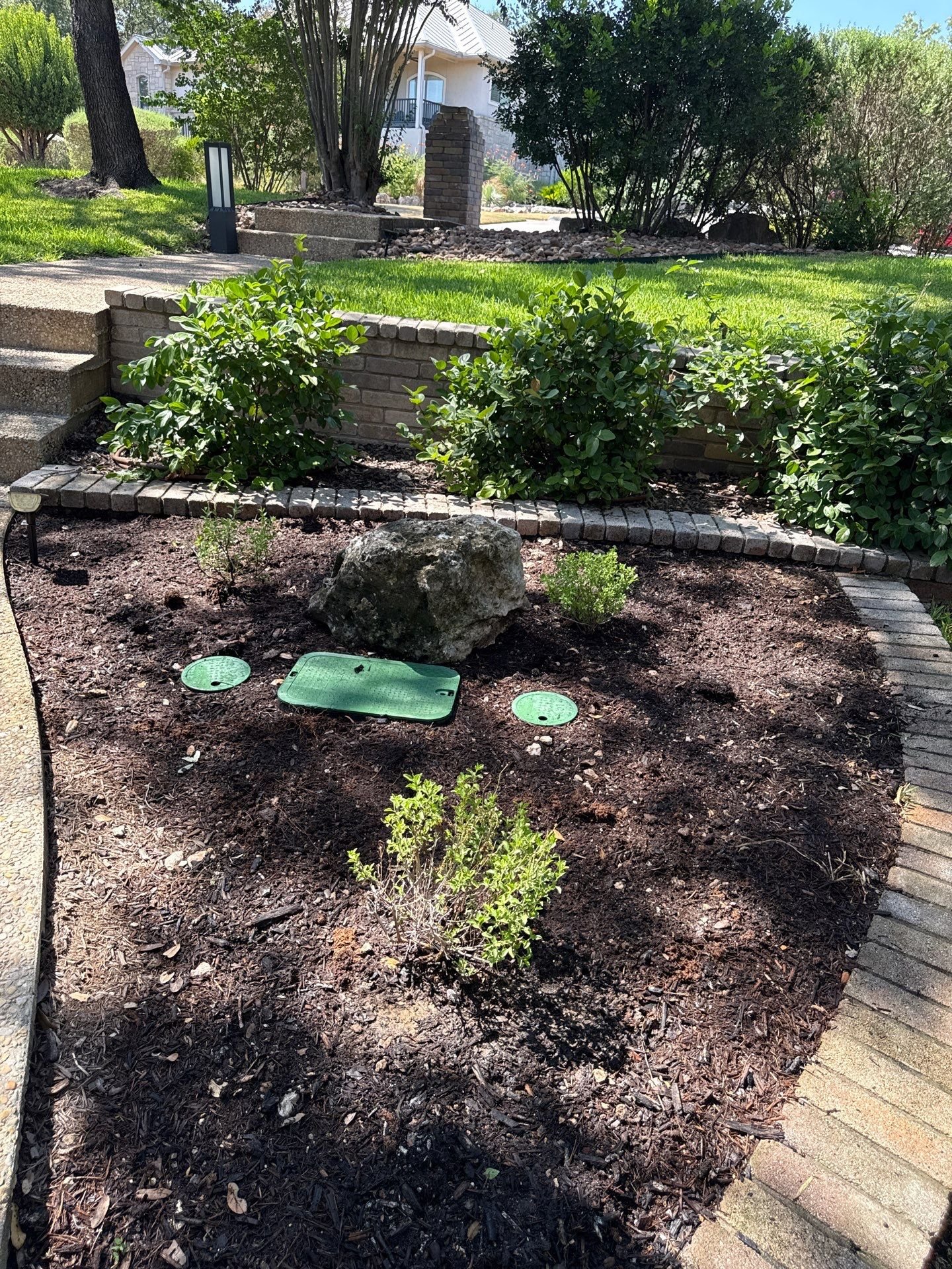 Mulched shrub bed with paver edging next to limestone retaining wall and steps in Fair Oaks Ranch, TX