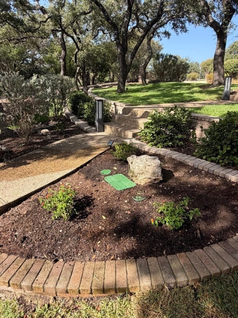 Curved paver-bordered planting bed with boulder and mulch below limestone steps in Fair Oaks Ranch, TX