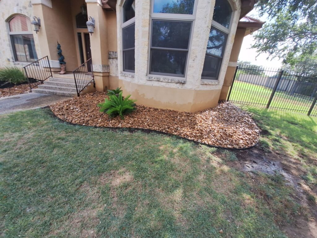 River rock foundation bed with accent shrub wrapping a stucco home's bay window in Garden Ridge, TX