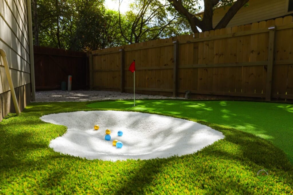 Synthetic putting green with white sand bunker and flag in a fenced Helotes, TX backyard
