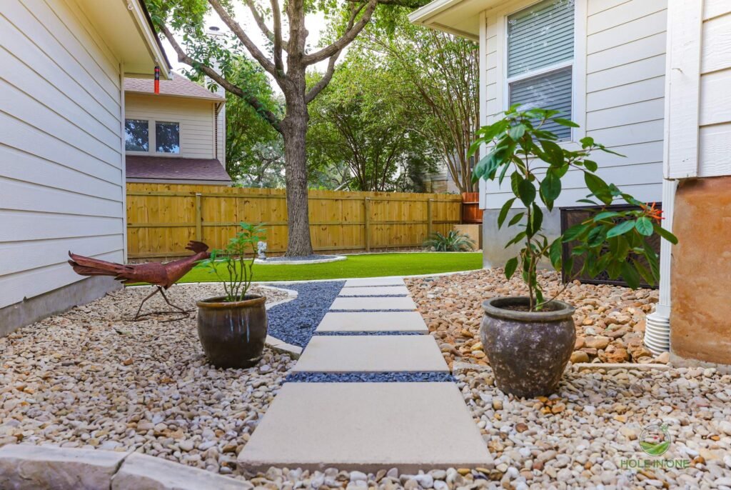 Side-yard concrete stepping pads in river rock leading to a turf lawn in Helotes, TX