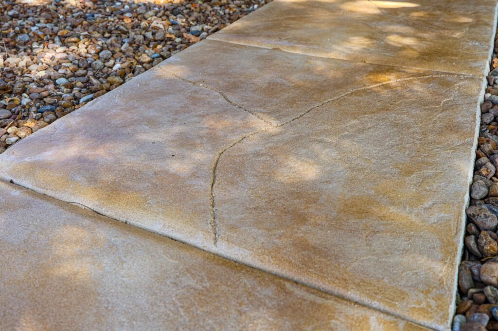 Scored and stained concrete entry walkway bordered by river rock beds at a New Braunfels, TX home