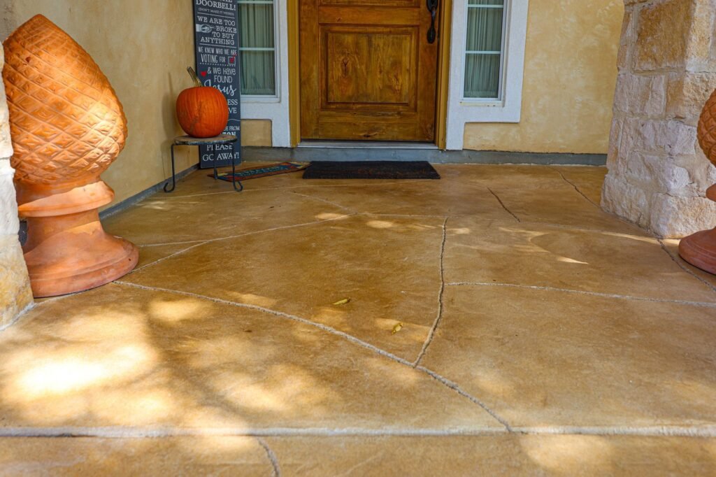Stained flagstone-pattern concrete overlay on a front porch with limestone columns in New Braunfels, TX