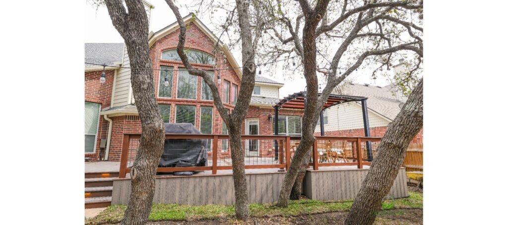 Raised Trex deck with skirting, wire railing and pergola behind a two-story brick home