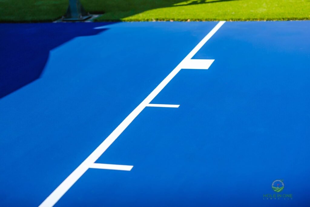 Close-up of crisp white painted lane lines on a blue acrylic sport court surface next to artificial turf