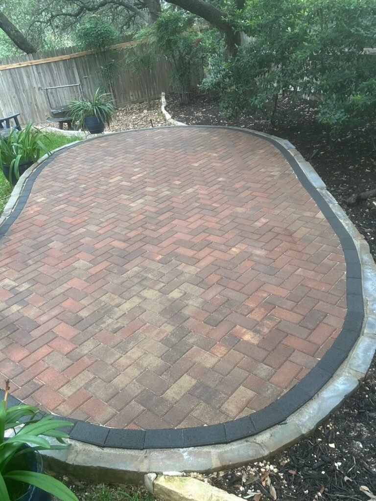 Oval herringbone clay-brick paver patio with charcoal border under mature trees in North San Antonio