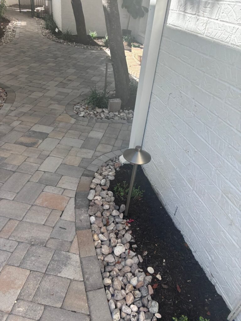Curving paver path, river rock edging and landscape lighting beside a mulched bed in Terrell Hills, TX